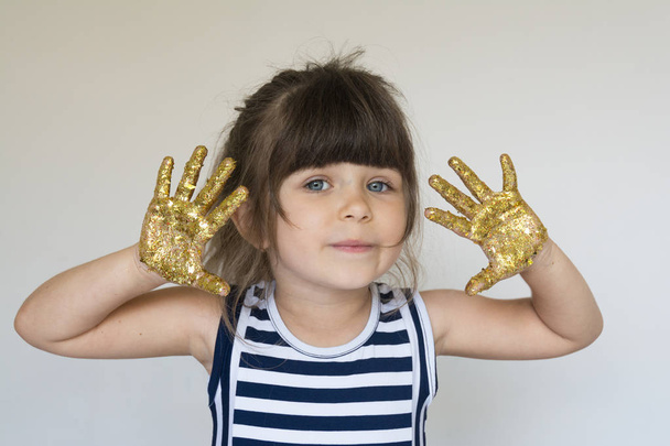 Красива маленька дівчинка з руками в золотій фарбі
. - Фото, зображення