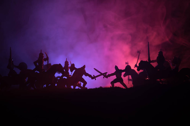 Escena de batalla medieval con caballería e infantería. Siluetas de figuras como objetos separados, lucha entre guerreros sobre fondo de niebla tonificado oscuro. Escena nocturna. Enfoque selectivo
 - Foto, Imagen