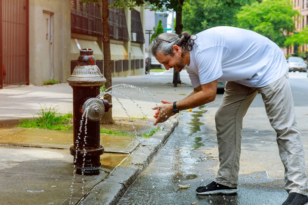 Mężczyzna w średnim wieku podczas silnego cieplna jest odświeżany z wodą z hydrantu - Zdjęcie, obraz