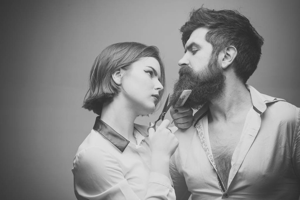 Barbershop or hairdresser concept. Woman hairdresser cuts beard with scissors. Man with long beard, mustache and stylish hair, light background. Guy with modern hairstyle visiting hairdresser. - Photo, Image