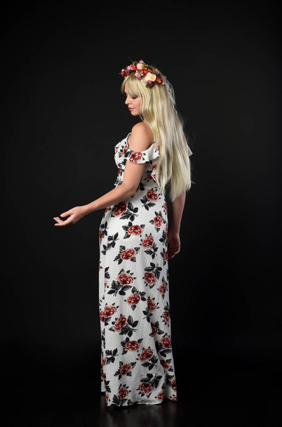 full length portrait of blonde girl wearing floral dress, standing pose on black studio background. - Photo, Image