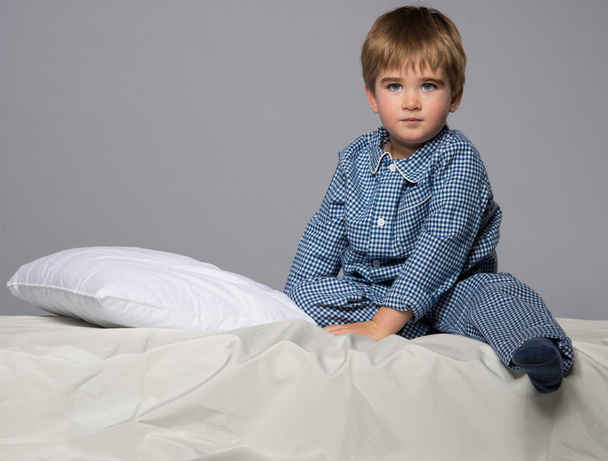 男の子がベッドの中で青いパジャマを着ています。 - 写真・画像