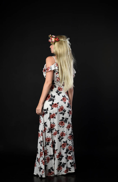портрет повної довжини блондинки в квітковій сукні, стоячи позу на чорному студійному фоні
. - Фото, зображення