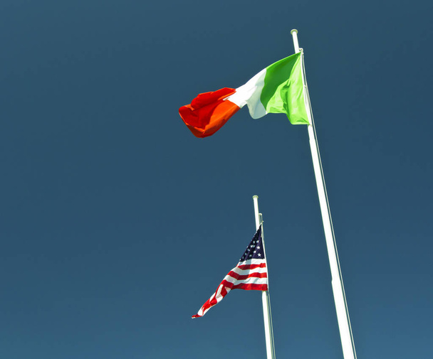 青空の背景として使うと風になびかせてイタリアとアメリカの旗. - 写真・画像