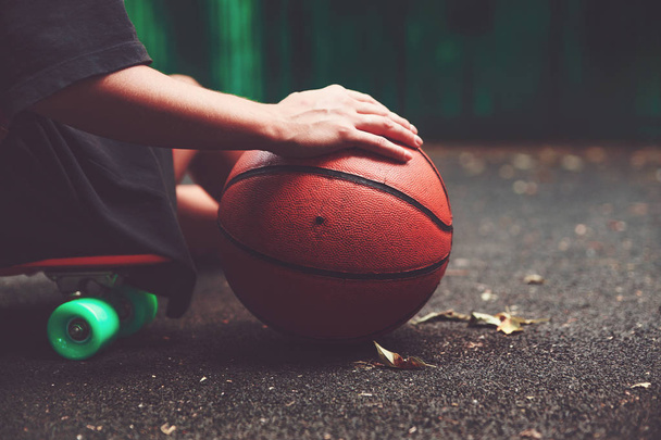 Closeup photo basketball ball with girl sitting on plastic orange penny shortboard on asphalt  - Foto, Imagem