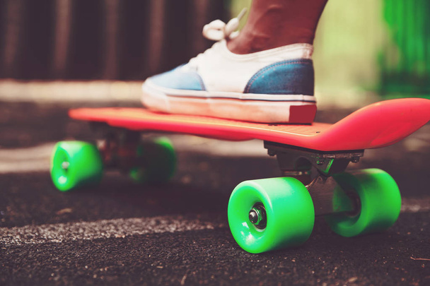 Close up of feet of girl sneakers rides on orange penny skateboard on asphalt - Фото, изображение