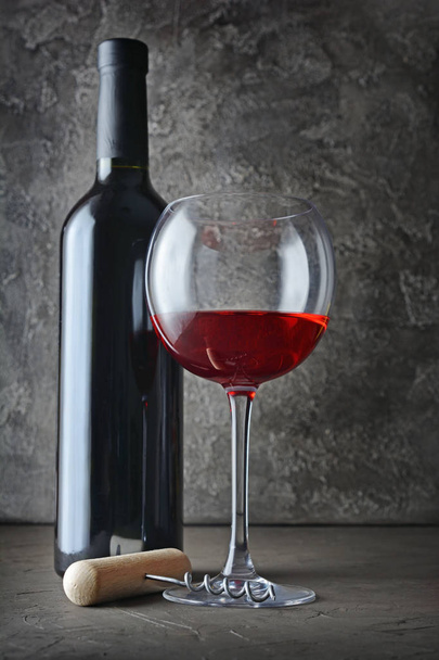 Botella de vino tinto y copa para degustación con sacacorchos en bodega oscura sobre fondo de hormigón gris
 - Foto, Imagen