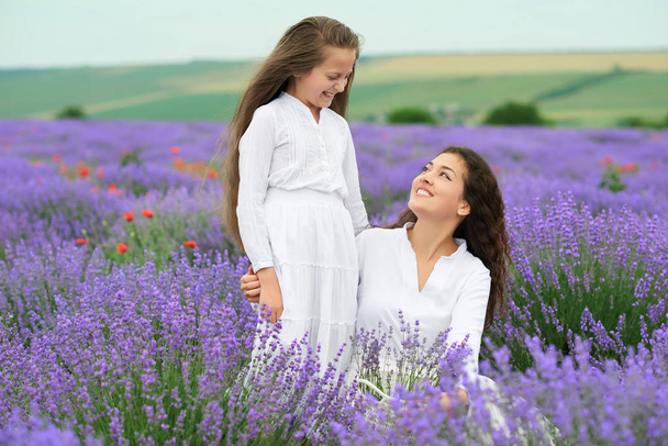 jonge vrouw en een meisje zijn op het gebied van lavendel, mooie zomerse landschap met rode klaproos bloemen - Foto, afbeelding