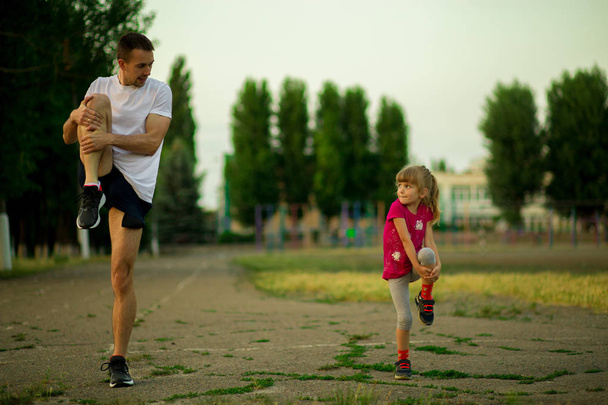 Athletic young father and little daughter do exercises in stadium. Healthy lifestyle - Photo, Image