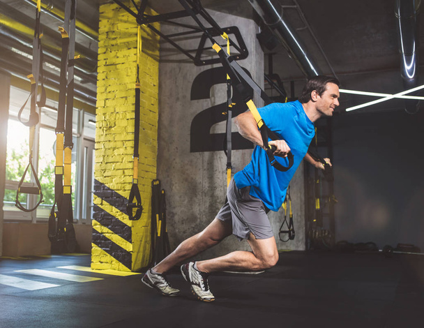 Positive man taking exercise with trx - Foto, imagen