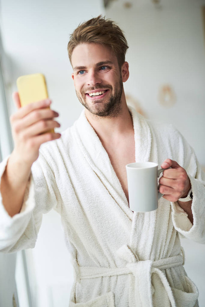 Delighted man making selfie in hotel in morning - 写真・画像