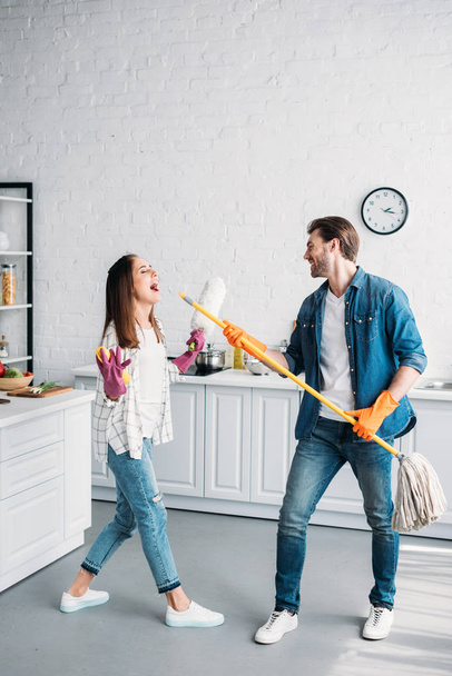 pareja en guantes de goma divirtiéndose con fregona y fingiendo cantar en la cocina
 - Foto, imagen
