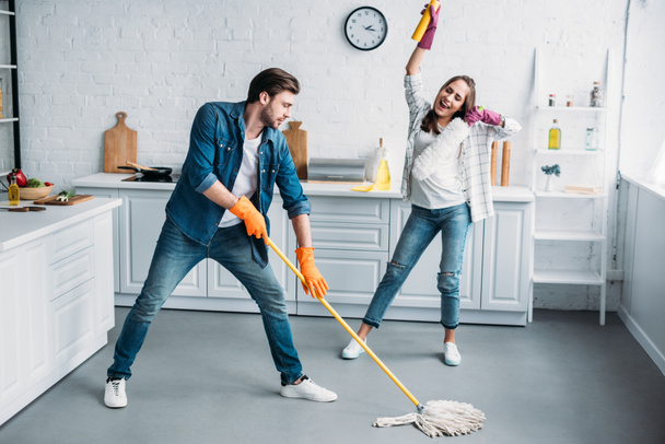 couple in rubber gloves having fun with mop during cleaning kitchen - Foto, afbeelding