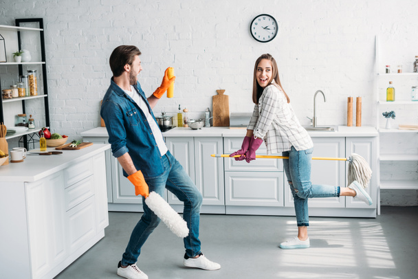 пара в резиновых перчатках весело провести время со шваброй на кухне
 - Фото, изображение