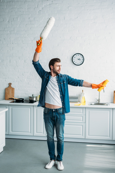 man posing with dust brush and cleaner in kitchen - Фото, изображение