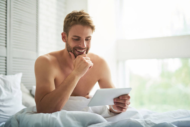 Handsome man rubbing chin during conversation online at home  - Photo, image