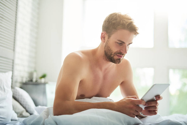 Handsome serious man surfing net in bed - Фото, изображение