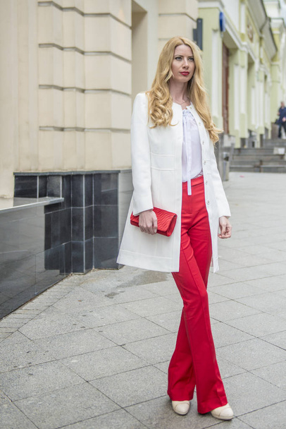 Fashionable young blonde in a spring fashionable suit and with a shopping bag in the center of Moscow - Фото, изображение