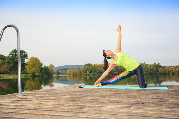 young woman doing yoga exercise at a lake - Foto, Imagem