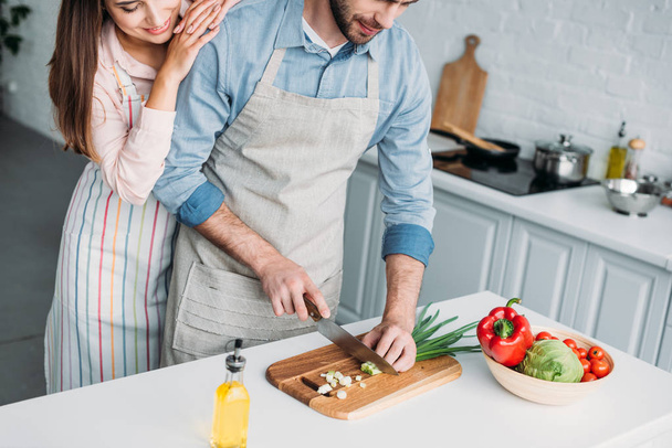 cropped image of boyfriend cutting vegetables and girlfriend leaning on him in kitchen - Foto, Bild