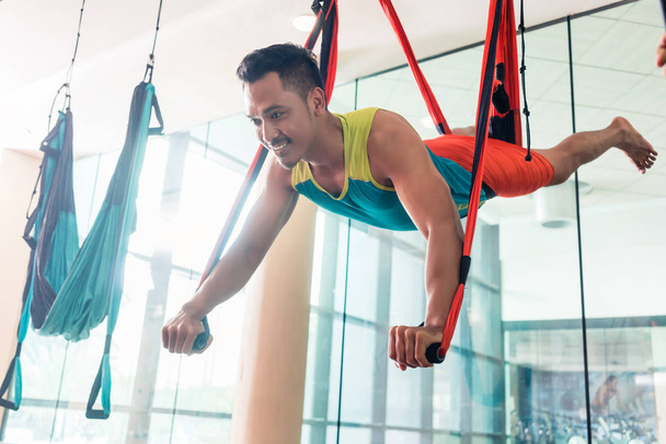 Fit handsome man smiling while practicing anti-gravity yoga - Photo, Image