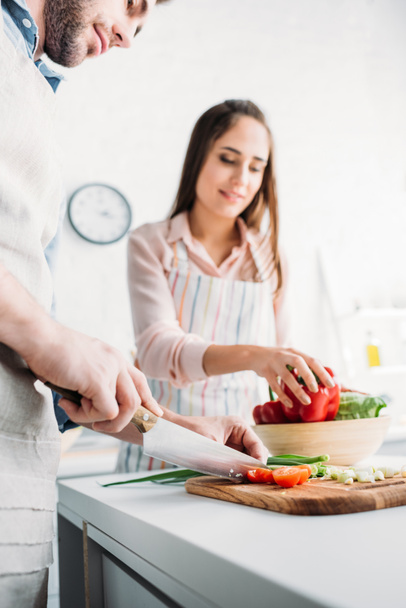boyfriend cutting vegetables and girlfriend taking bell pepper in kitchen - Foto, Imagen