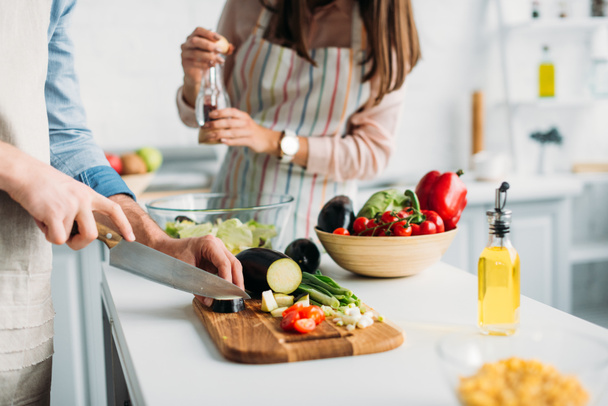 imagen recortada de novio cortar ingredientes y novia añadir especias a la ensalada en la cocina
 - Foto, Imagen