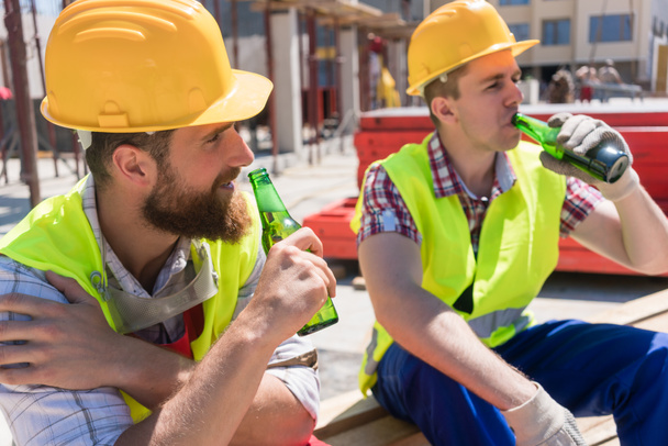 Kaksi nuorta työntekijää juomassa kylmää olutta tauolla töissä
 - Valokuva, kuva