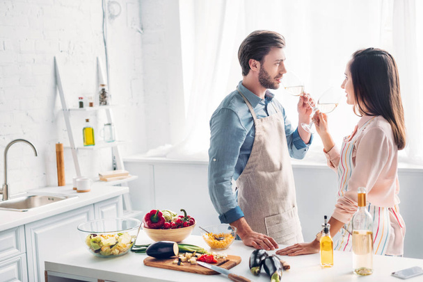 couple drinking wine and looking at each other in kitchen - Photo, Image