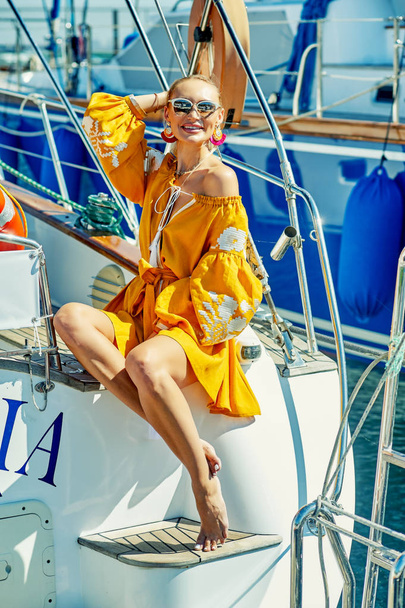 Ελκυστική νεαρή γυναίκα σε ένα γιοτ σε μια καλοκαιρινή μέρα. Όμορφη μόδας γυναίκα στο καλοκαίρι υπαίθρια., νεαρή γυναίκα ευτυχισμένη στο φόντο των σκαφών στη θάλασσα. - Φωτογραφία, εικόνα