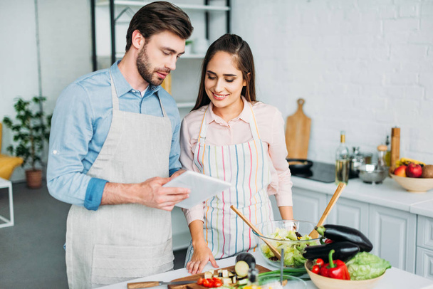 couple looking at tablet with recipe while cooking in kitchen - Foto, Bild