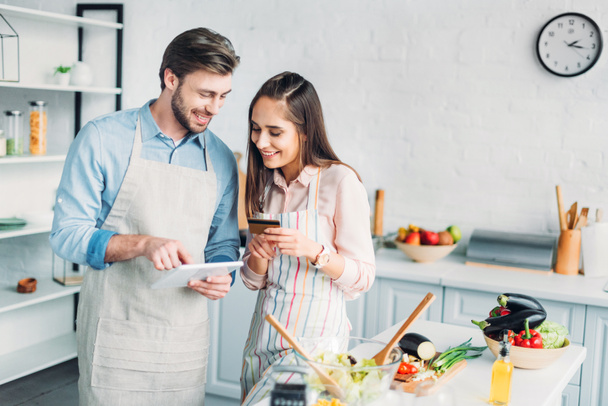 happy couple shopping online with tablet and credit card in kitchen - Photo, Image