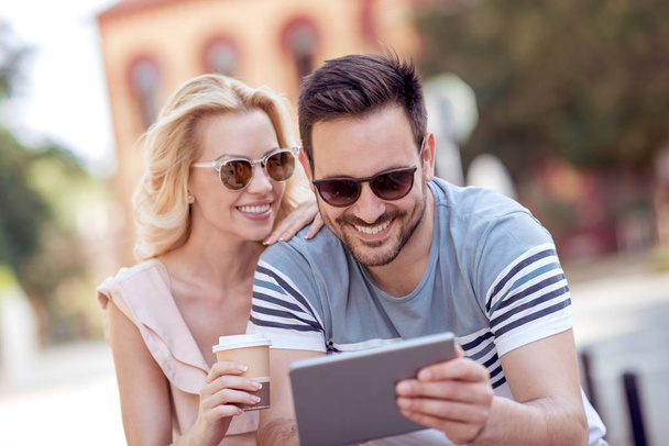 Hombre y mujer tomando café y sentados en el parque de la ciudad y usando la tableta
. - Foto, Imagen