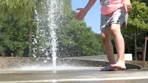 Zwolnionym tempie. Dziewczynka boso nogi grać z biczami wodnymi fontanna. Summertime przyjemność.  - Materiał filmowy, wideo