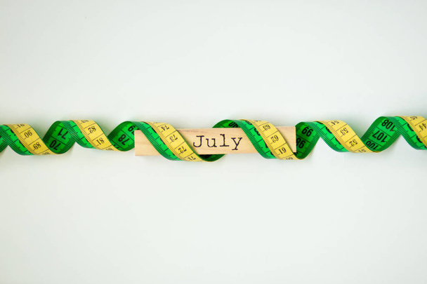 wooden calendar set on july with centimeter tape isolated on white background - Photo, Image