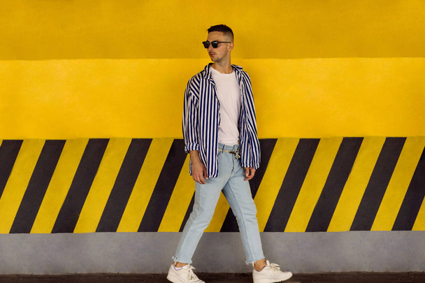 fashion guy in a striped shirt is standing near a yellow parking wall - Fotoğraf, Görsel
