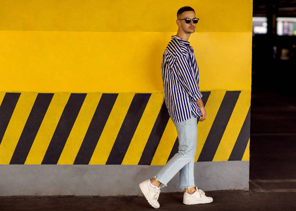 fashion guy in a striped shirt is standing near a yellow parking wall - Foto, Imagem