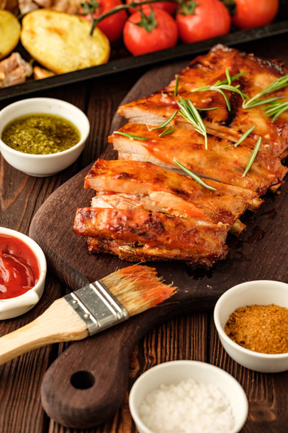 Delicious barbecued ribs seasoned with a spicy basting sauce and served with chopped fresh vegetables on an old rustic wooden chopping board. - Foto, Imagem