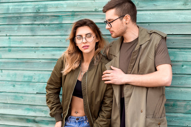 Модная пара, стоящая возле зеленой деревянной стены
 - Фото, изображение