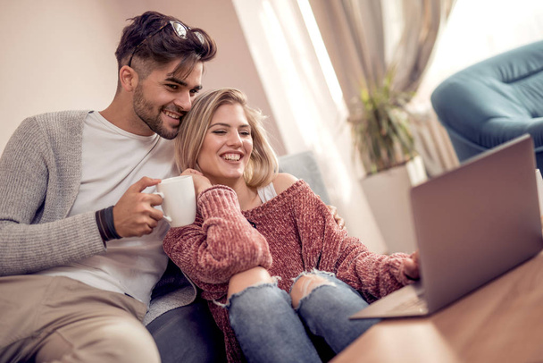 Paar sitzt auf Sofa, trinkt Kaffee und benutzt Laptop zu Hause - Foto, Bild