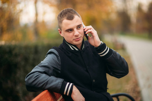 ein junger Mann in schwarzer Jacke telefoniert - Foto, Bild
