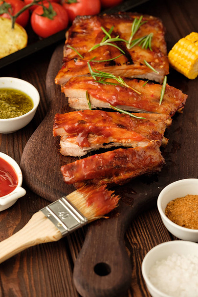 Delicious barbecued ribs seasoned with a spicy basting sauce and served with chopped fresh vegetables on an old rustic wooden chopping board - Foto, Imagem
