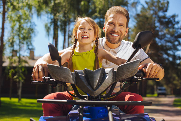 Smiling girl driving ATV with her daddy - Foto, Bild