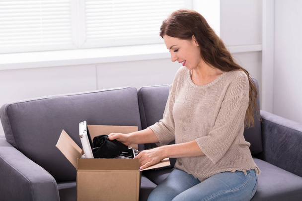 Smiling Young Woman Sitting On Sofa Unpacking Received Parcel - Foto, Imagen