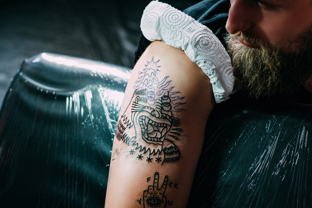 vista parcial del hombre con nuevo tatuaje en el hombro en el salón de tatuajes
 - Foto, Imagen