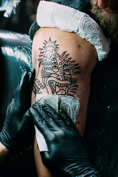 vista parcial del artista del tatuaje en guantes trabajando en tatuaje en el hombro en el salón
 - Foto, Imagen