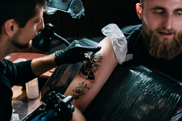 enfoque selectivo del artista del tatuaje en guantes que trabajan en el tatuaje en el hombro en el salón
 - Foto, Imagen