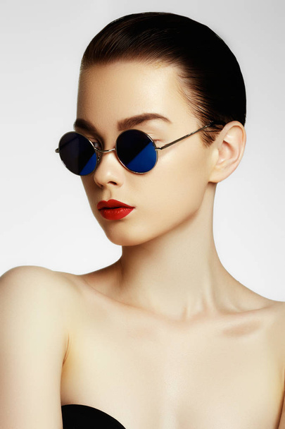Ομορφιά πορτρέτο της όμορφο μοντέλο μελαχρινή γυναίκα με το κομψό χτένισμα σε γυαλιά ηλίου. Επαγγελματικό μακιγιάζ. Μοντέλο μόδας στα γυαλιά ηλίου. Μόδα και αξεσουάρ - Φωτογραφία, εικόνα