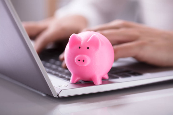 Businessperson's Hand Working On Laptop With Pink Piggybank - Foto, imagen