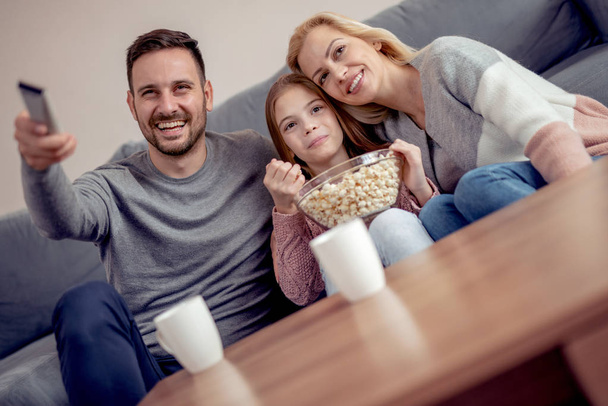 Nuori perhe katsomassa televisiota yhdessä kotona ja hauskaa yhdessä
. - Valokuva, kuva